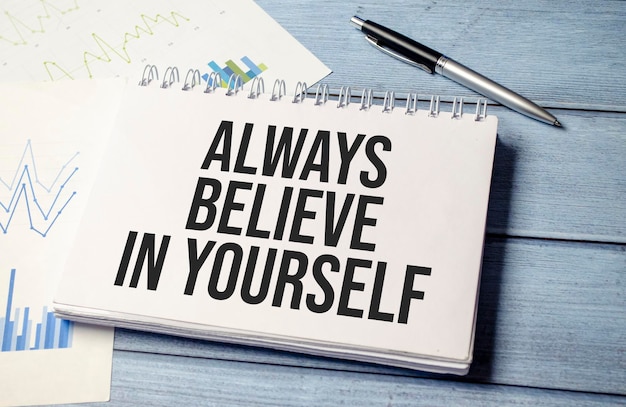 Photo always believe in yourself text on blue wooden background with charts and pen