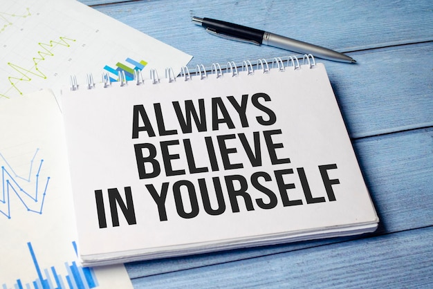 ALWAYS BELIEVE IN YOURSELF text on blue wooden background with charts and pen