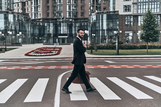 Фото Всегда осторожно. молодой человек в полный рост в полном костюме, переходящий улицу