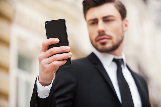 Always connected. Confident young man in formalwear holding mobile phone while standing outdoors