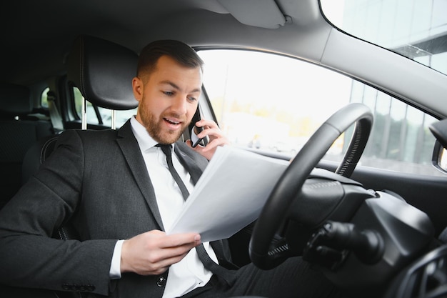 いつも急いで車を運転しながら笑顔のフルスーツのハンサムな若い男