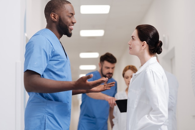 Always open to other opinions. Smiling proficient charming practitioners enjoying coffee break in the hospital and expressing positivity while sharing ideas