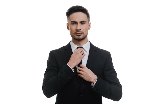 Always perfect. Handsome young man in full suit adjusting his necktie and looking at camera