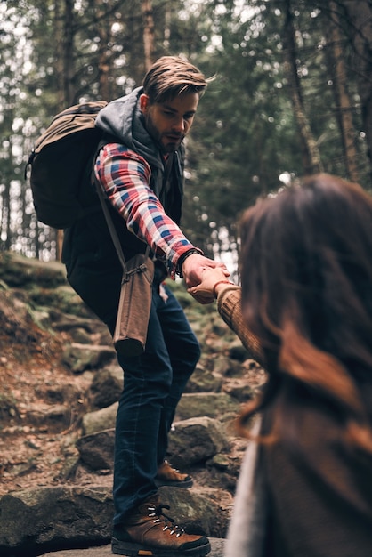 Always ready to help. Modern young couple holding hands and moving up while hiking together in the woods