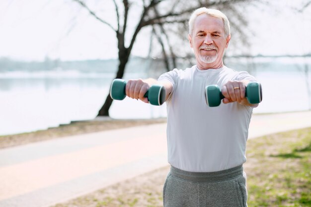 Photo always in shape. energetic mature man rising dumbbells and staring down