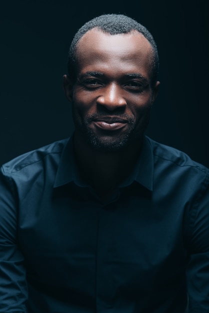 Always stay real! Portrait of handsome young African man looking at camera with smile while being in front of black background