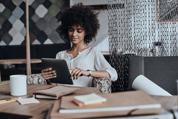 Photo always taking care of business. beautiful young african woman in smart casual wear working using digital tablet while sitting in cafe or creative office