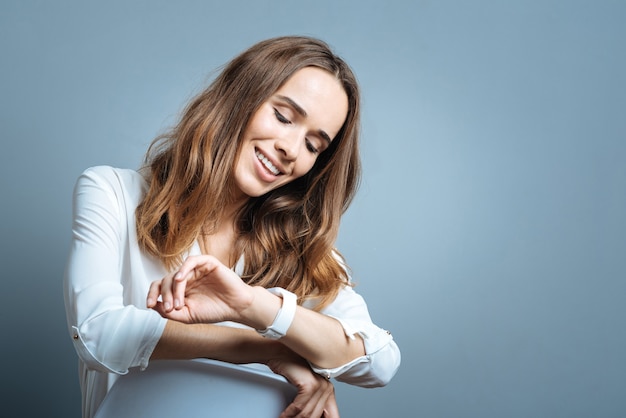 Always in time. Positive delighted cheerful woman smiling and looking at her watch while wanting to know the time