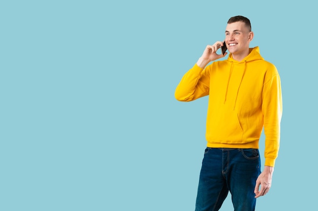 青い背景のバナーの上にポーズをとるコピースペースを見て、スマートフォンで話しているカジュアルな白人男性