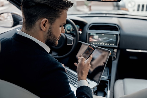 Always in touch. Top rear view of young man in formalwear using his smart phone while sitting in the car