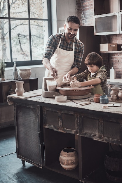 Always up for learning from father. Cheerful young man and little boy making ceramic pot on the pottery class