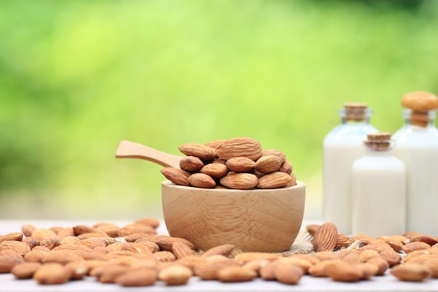 Amandel in een kom en amandelmelk in glazen fles op de tafel wazig natuurlijke groene achtergrond