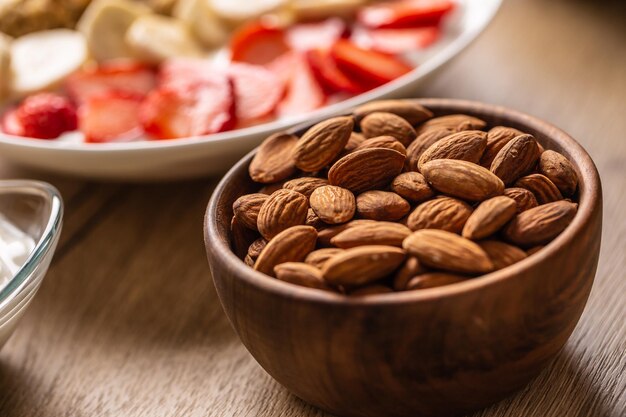 Foto amandelen in een houten schaal met yoghurt en een bord gezond ontbijt