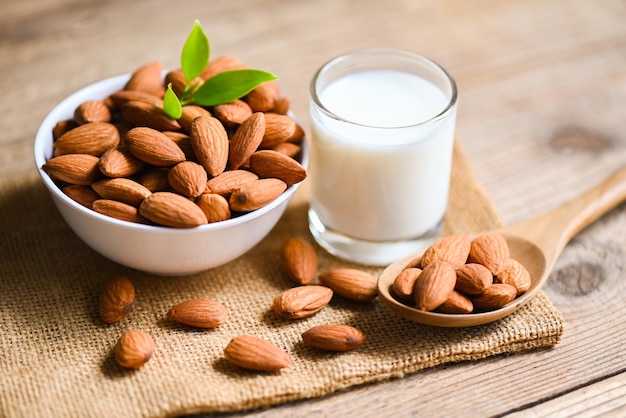 Amandelmelk en amandelen noten op witte kom met groen blad op zak achtergrond heerlijke zoete amandelen op de houten tafel geroosterde amandelnoot voor gezonde voeding en snack