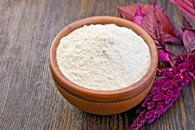 Amaranth flour in a clay bowl, purple amaranth flower on the background of wooden boards