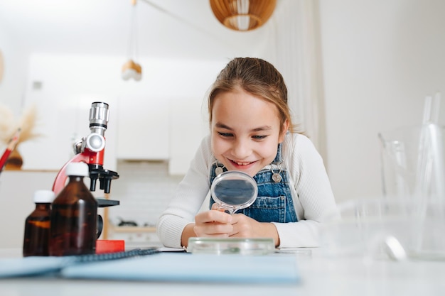 Amased little girl doing home science project, looking through magnifying glass