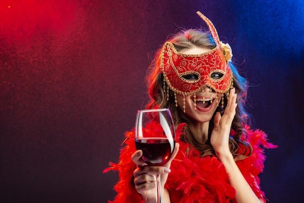 Amasing donna in una maschera di carnevale rosso e boa con un bicchiere di vino alzato.