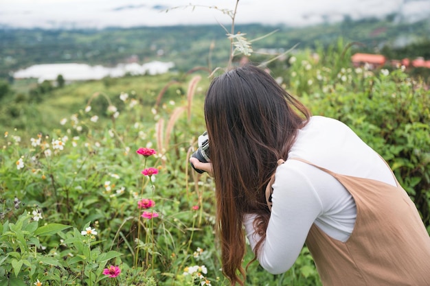 Amateur aziatische vrouw die foto's maakt met retro filmcamera tussen de bloementuinaard op het platteland