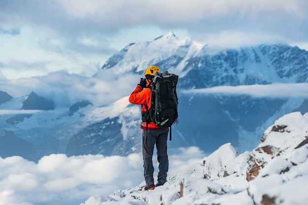 An amateur mountaineer photographer with a large backpack on his shoulders captures the view of beautiful snow-capped mountains with glaciers on the camera.mountain