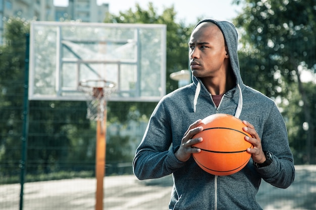 Amateur player. Serious young man looking at the basketball court while coming there to play