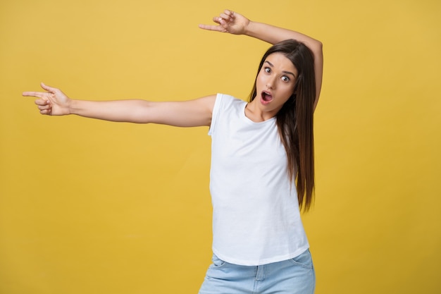 Amaze young woman pointing to one side with her finger while opening her mouth against a yellow background