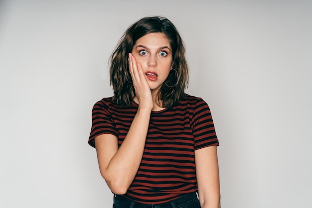 Amazed adult pretty female touching cheek in studio