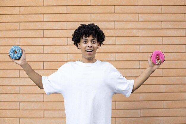 Amazed American guy wearing a white Tshirt holding chocolate and blue donuts on each side