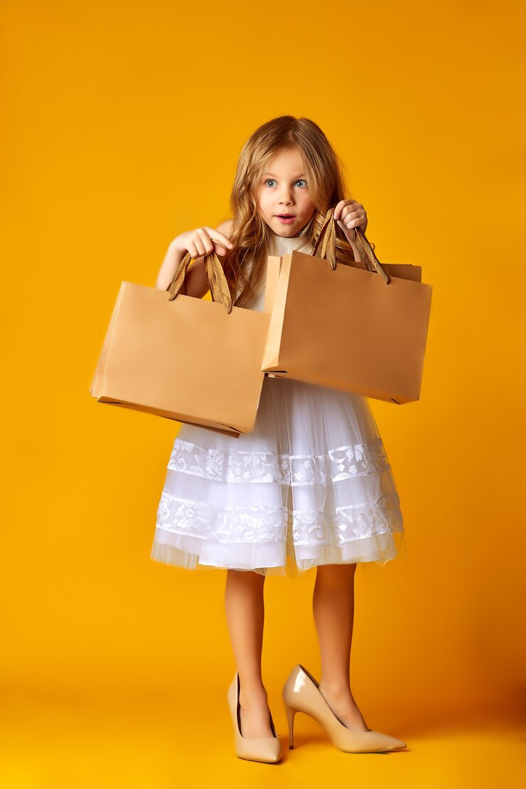 Photo amazed attractive child in dress and big shoes holding shopping bags