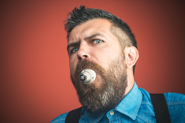 Amazed bearded man holding light bulb in teeth man with beard and mustache in denim shirt holds