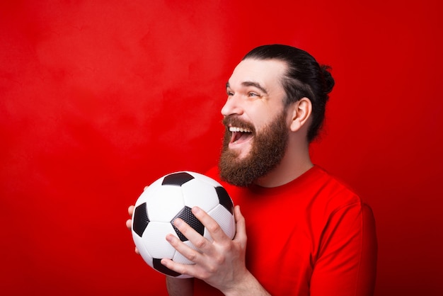 Amazed bearded man holding soccer ball and supporting his team