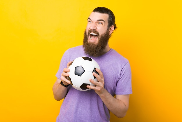 Amazed bearded man screaming and celebrating victory and holding soccer ball