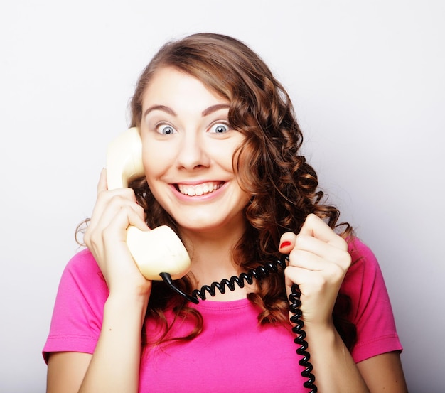 Amazed beautiful curly woman talking on white vintage telephone isolated over white background