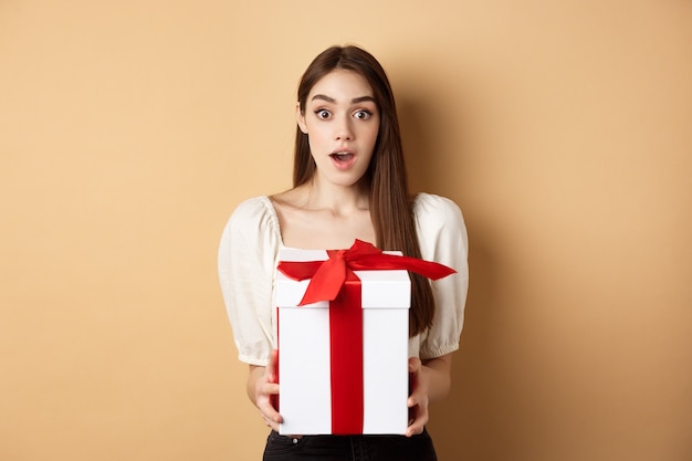 Amazed beautiful girl receiving gift from secret admirer on valentines day looking surprised at came.