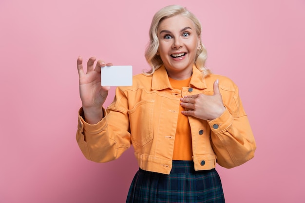 Photo amazed blonde woman holding empty driving license isolated on pink