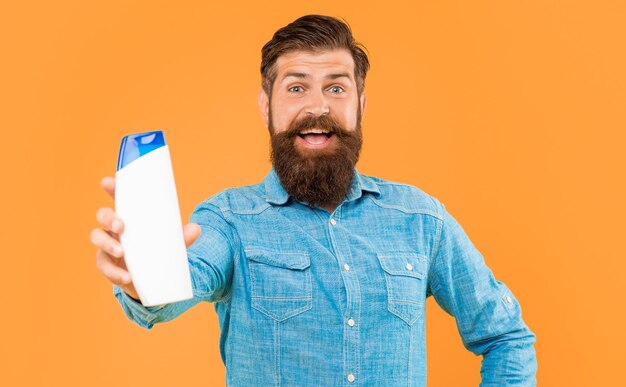 Amazed brutal bearded man hold shampoo bottle on yellow background haircare