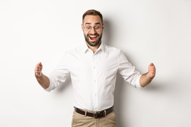 Amazed businessman showing big object, describe something large and looking excited, standing over white background.