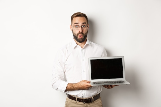 Amazed businessman showing laptop screen, standing against white background.