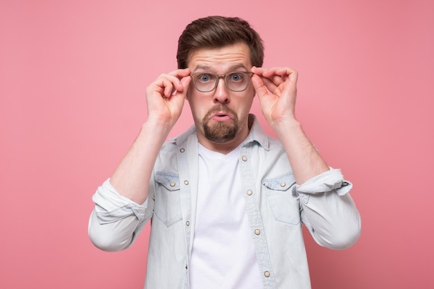 Amazed caucasian young man looking at camera through glasses