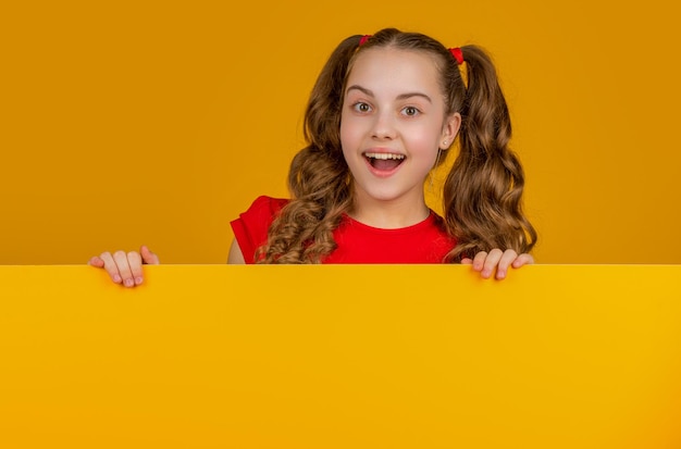 Photo amazed child behind blank yellow paper with copy space for advertisement