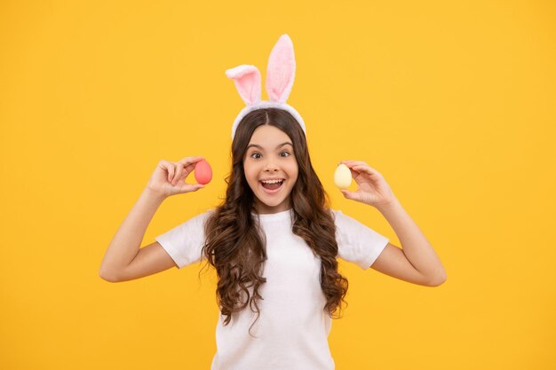 Amazed child in bunny ears hold eggs on yellow background, happy easter