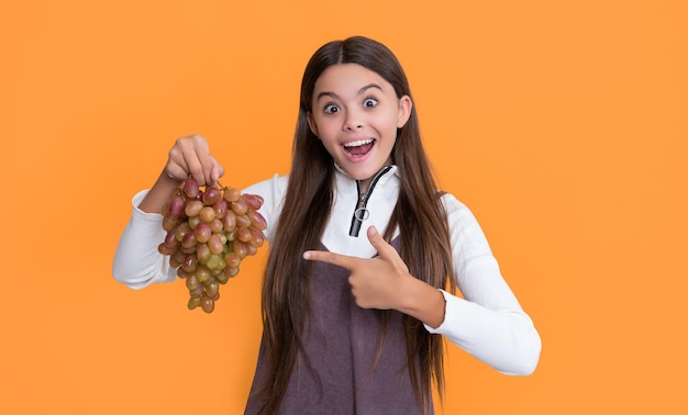 Amazed child holding fresh grapes fruit on yellow background