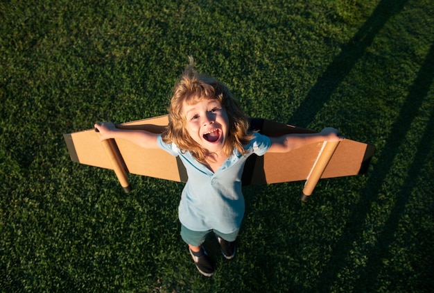 Удивленный ребенок, играющий с крыльями игрушечного самолета в летнем парке, инновационные технологии и концепция успеха e