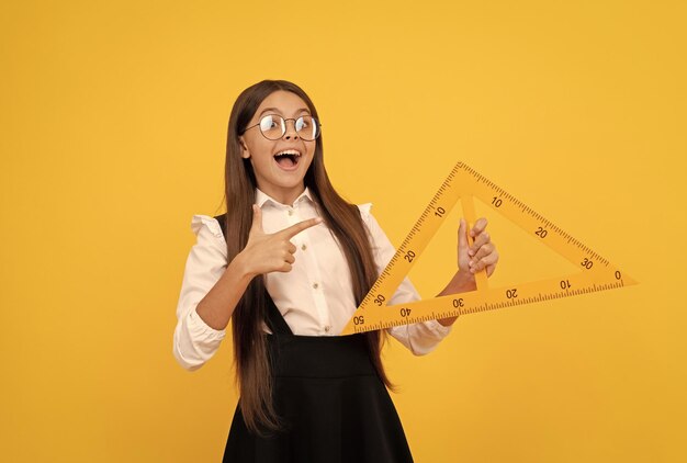 Amazed child in school uniform and glasses hold mathematics triangle for measuring trigonometry