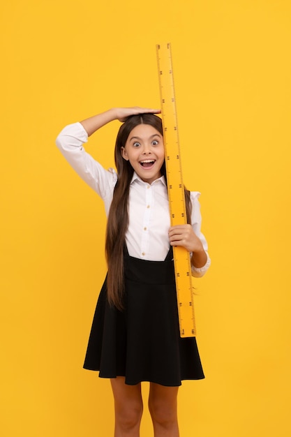 Amazed child in school uniform hold mathematics ruler for measuring height