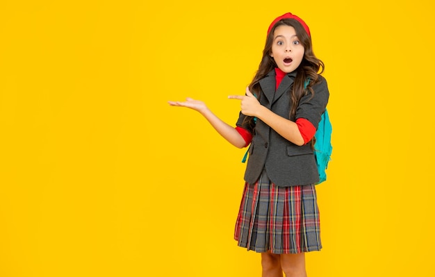 Amazed child in school uniform with backpack pointing finger on copy space education