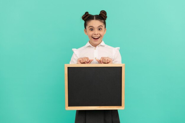 Amazed child in school uniform with blackboard on blue background, copy space, advertisement