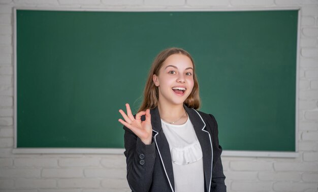 Amazed child standing on blackboard background in classroom at school ok