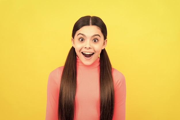 Amazed child with long hair on yellow background surprise