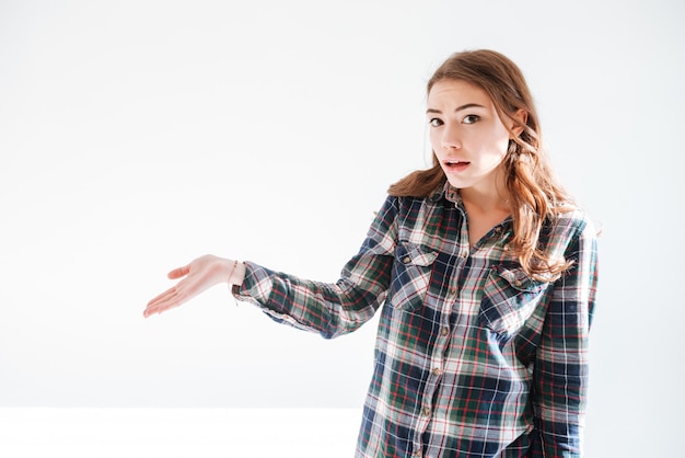 Amazed confused woman in plaid shirt holding copyspace on palm