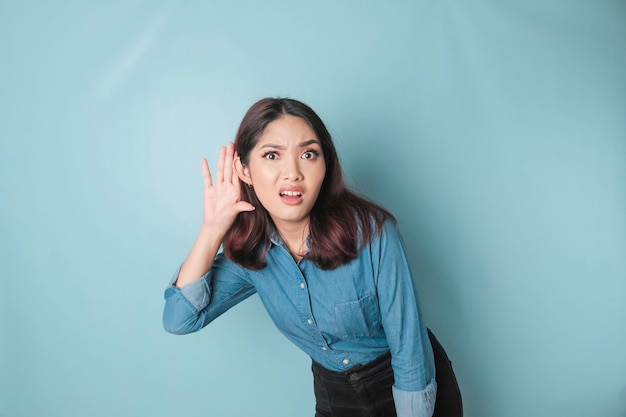 Amazed curious bride young woman wearing a blue shirt trying to hear you overhear listening intently isolated on blue turquoise background studio portrait